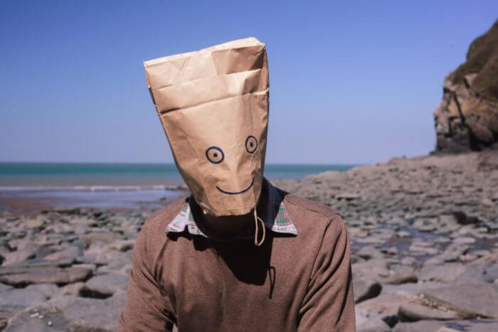 Man at beach with paper bag over his head