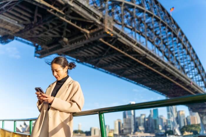Woman using phone app under Sydney Harbour Bridge