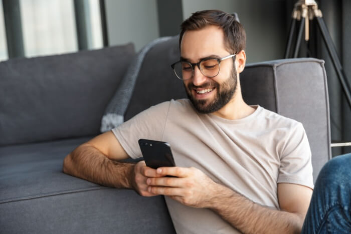 Man sitting beside couch smiling down at phone
